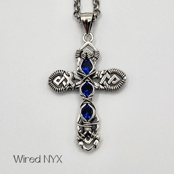 Blue Spinel (Lab Created) Wire Wrapped Cross Pendant in Sterling Silver (Oxidized) Material: Sterling Silver (Oxidized) Stones: Blue Spinel (Lab Created) Pendant height: 36mm Pendant width: 23mm Chain: Stainless Steel Round Rolo Chain (3mm) ~ Choose Length 18"-30" Inches