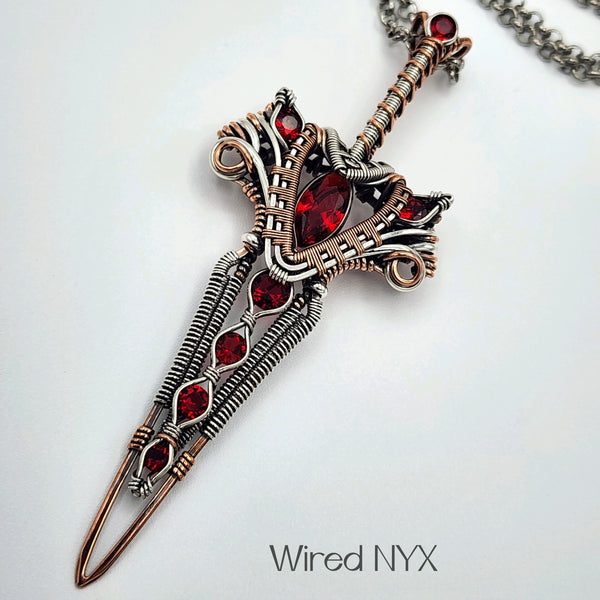 Simulated Ruby Wire Wrapped Sword Pendant in Sterling Silver/Copper (Oxidized) Material: Sterling Silver/Copper (Oxidized) Stones: Simulated Ruby Pendant height: 87mm Pendant width: 33mm Chain: Stainless Steel Round Rolo Chain (3mm) ~ Choose Length 18"-30" Inches